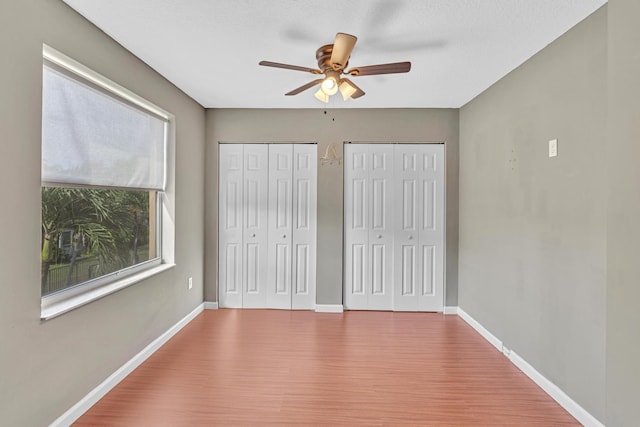 unfurnished bedroom with hardwood / wood-style floors, multiple closets, and ceiling fan