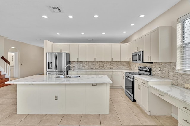 kitchen with light stone countertops, a kitchen island with sink, stainless steel appliances, and sink