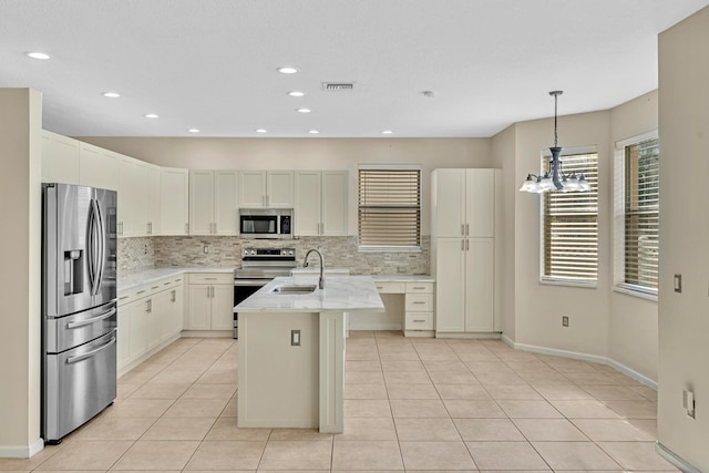 kitchen featuring light stone countertops, sink, stainless steel appliances, pendant lighting, and a center island with sink