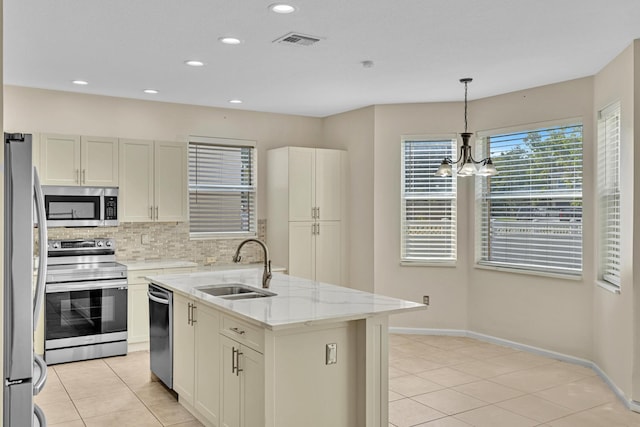 kitchen with decorative backsplash, hanging light fixtures, light stone counters, an island with sink, and stainless steel appliances