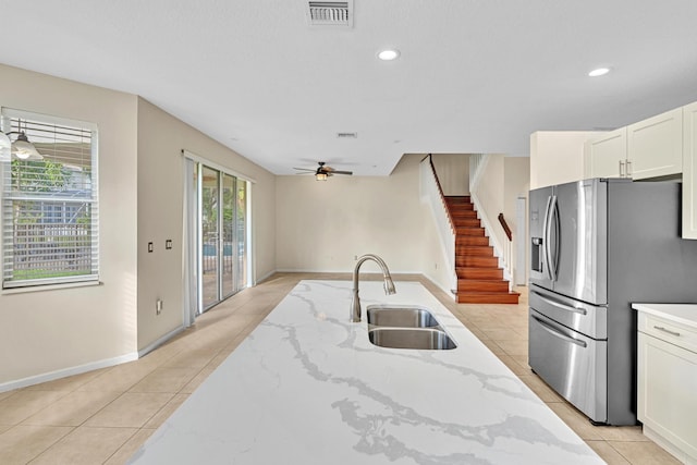 kitchen with sink, stainless steel fridge, white cabinetry, light stone counters, and ceiling fan