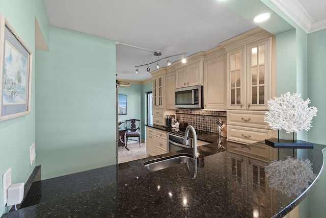 kitchen featuring cream cabinetry, ornamental molding, dark stone countertops, pendant lighting, and sink