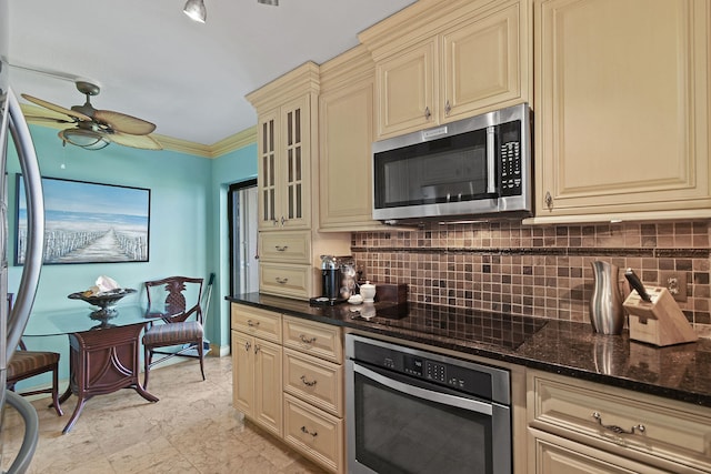 kitchen featuring cream cabinetry, ceiling fan, stainless steel appliances, dark stone counters, and ornamental molding