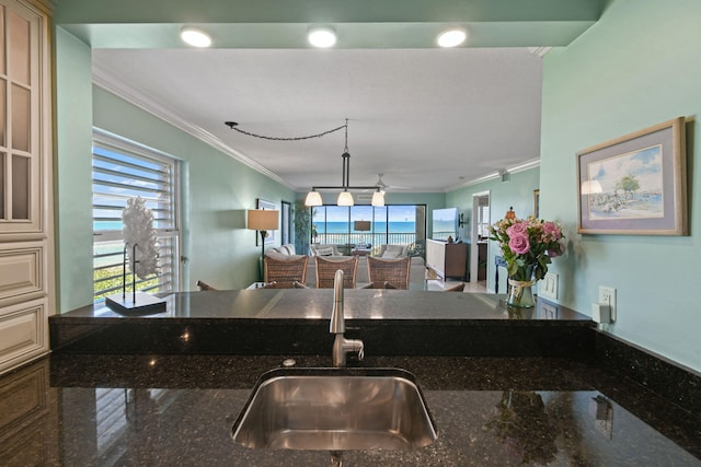 kitchen featuring dark stone counters, sink, crown molding, decorative light fixtures, and ceiling fan