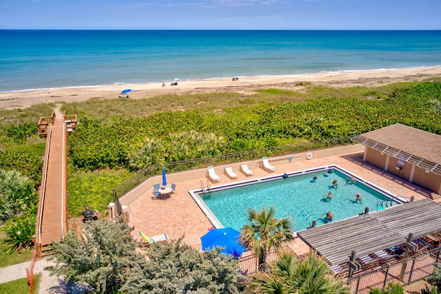 view of pool featuring a water view, a view of the beach, and a patio area