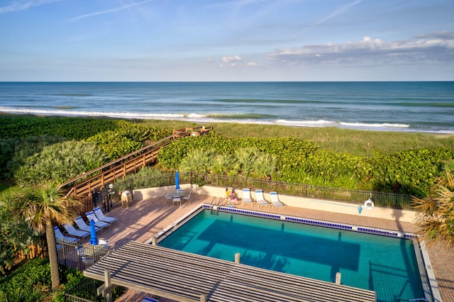 view of swimming pool with a water view, a patio, and a beach view