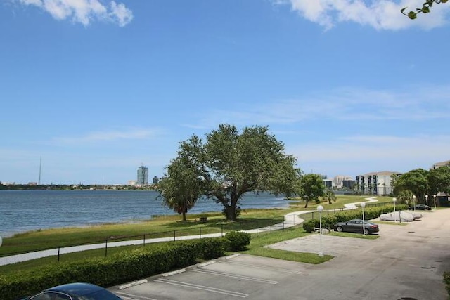 uncovered parking lot with a water view and fence