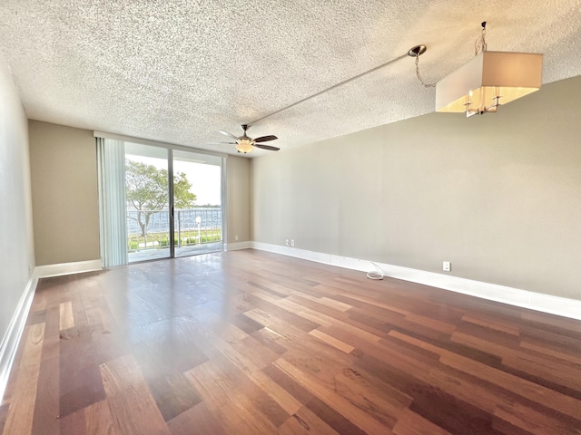 empty room featuring a textured ceiling, wood finished floors, a wall of windows, baseboards, and ceiling fan with notable chandelier