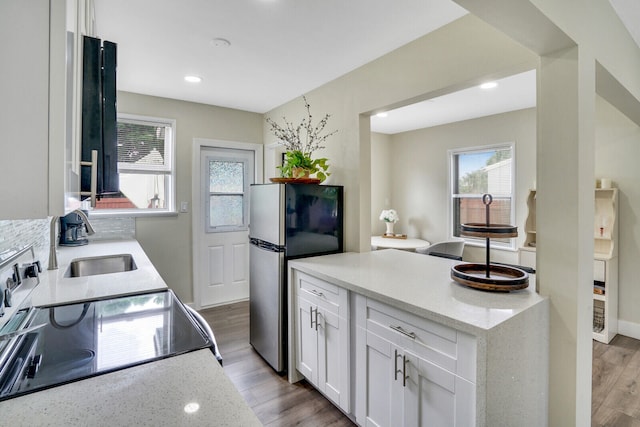 kitchen with light hardwood / wood-style floors, white cabinetry, light stone countertops, black range oven, and stainless steel fridge