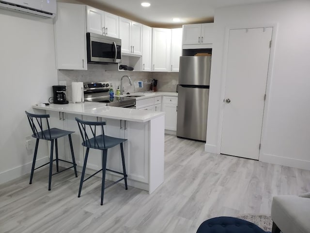 kitchen featuring an AC wall unit, appliances with stainless steel finishes, a kitchen bar, white cabinets, and kitchen peninsula