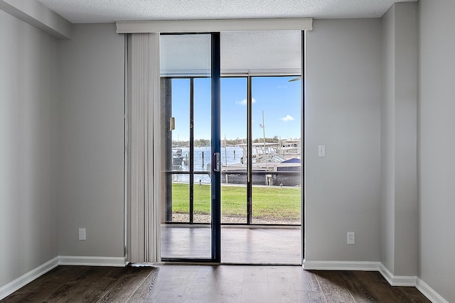 empty room with a water view, wood-type flooring, a textured ceiling, and expansive windows