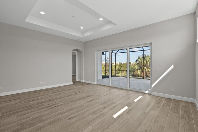 12501 SW Sunrise Lake Ter, Port Saint Lucie, FL 34987 - spare room with baseboards, light wood-type flooring, recessed lighting, arched walkways, and a tray ceiling