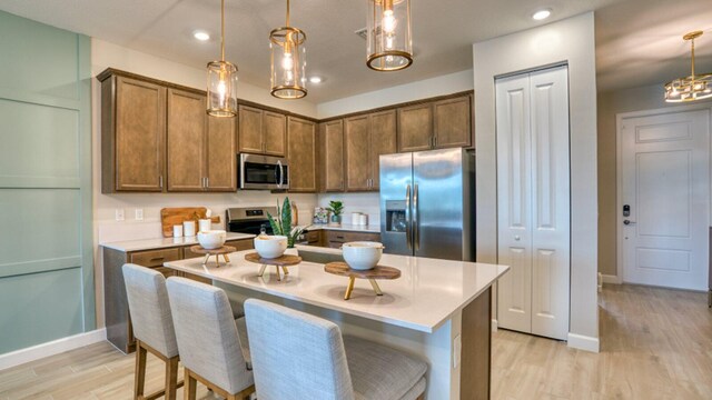 kitchen featuring light wood-type flooring, a kitchen bar, an island with sink, stainless steel appliances, and pendant lighting