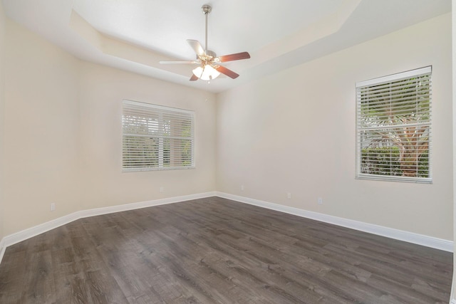 spare room featuring dark wood-type flooring, a healthy amount of sunlight, ceiling fan, and a tray ceiling