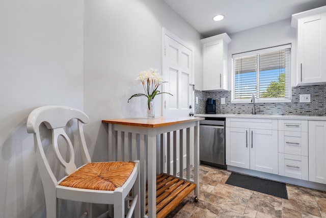 kitchen featuring wooden counters, sink, stainless steel dishwasher, white cabinetry, and tasteful backsplash