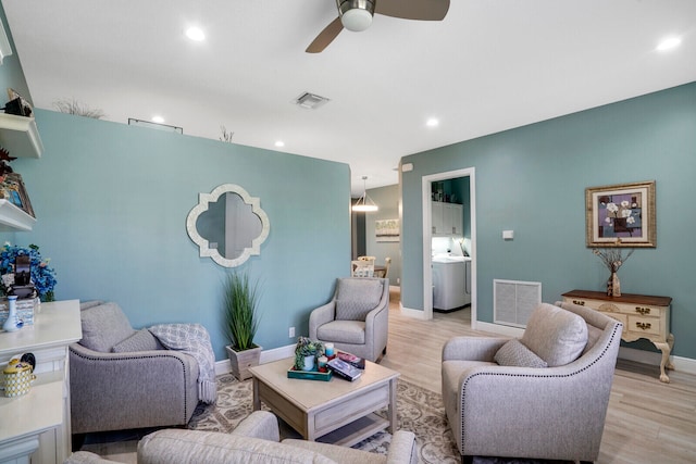 living room with washer / dryer, light hardwood / wood-style flooring, and ceiling fan