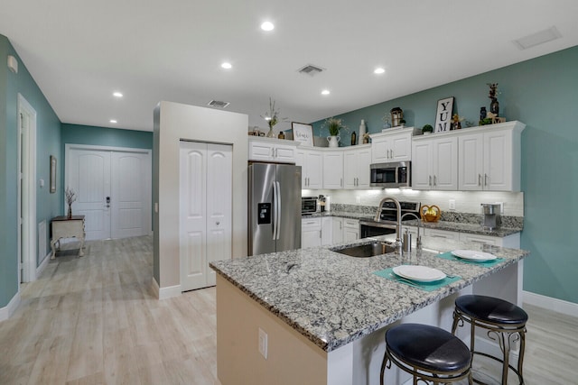 kitchen with white cabinets, light stone counters, a large island with sink, light wood-type flooring, and stainless steel appliances