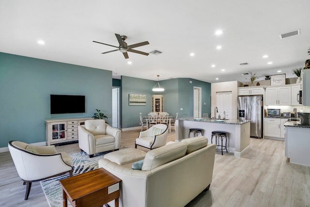 living room featuring sink, light hardwood / wood-style flooring, and ceiling fan