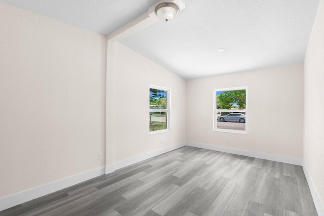 spare room featuring vaulted ceiling, a textured ceiling, and light wood-type flooring