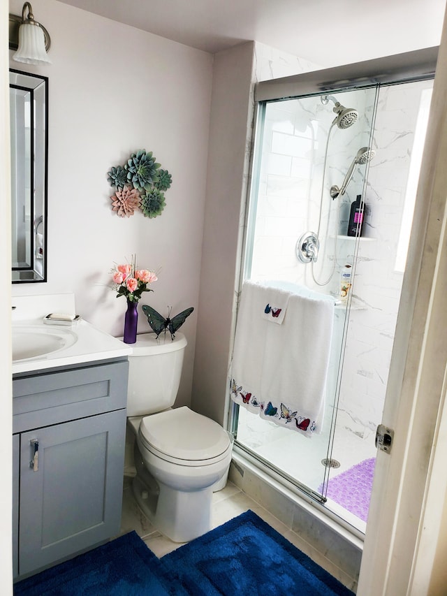 bathroom with a shower with door, vanity, toilet, and tile patterned floors