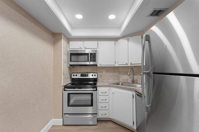 kitchen featuring appliances with stainless steel finishes, white cabinetry, a raised ceiling, and sink