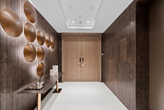 hallway with a tray ceiling and wood walls