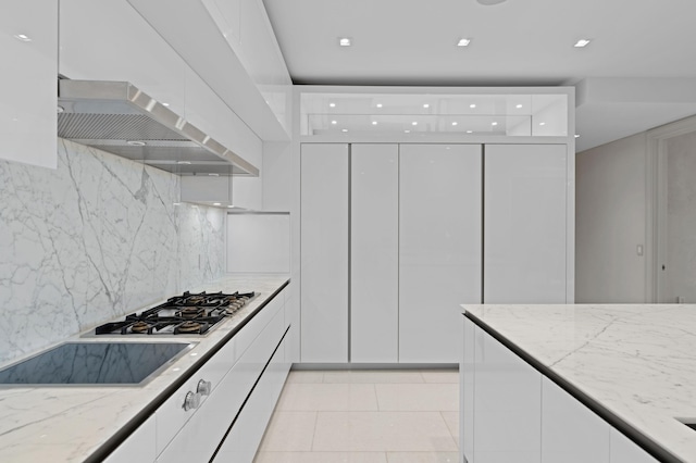 kitchen with stainless steel gas cooktop, white cabinetry, backsplash, light stone countertops, and wall chimney range hood