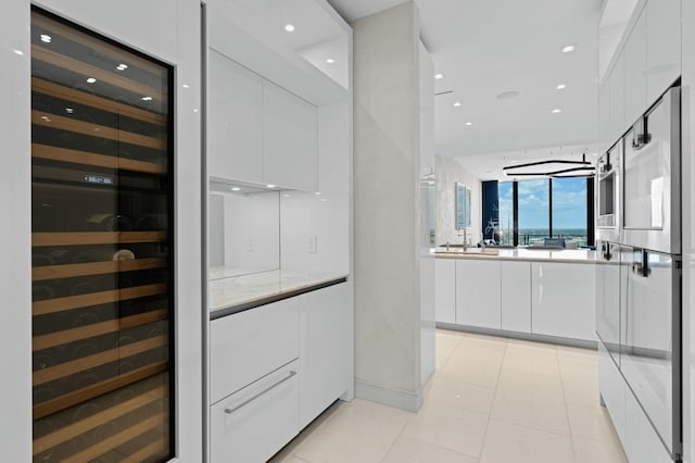 interior space featuring floor to ceiling windows, sink, light tile patterned floors, beverage cooler, and white cabinets