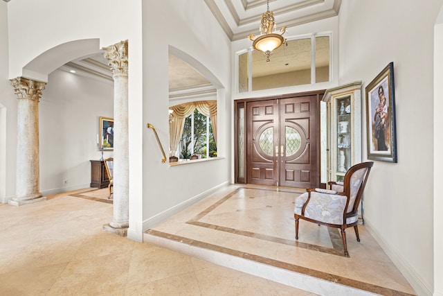 foyer featuring ornate columns, crown molding, a tray ceiling, and a high ceiling