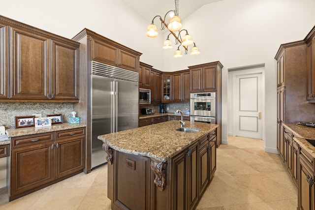 kitchen with decorative backsplash, built in appliances, an island with sink, decorative light fixtures, and high vaulted ceiling