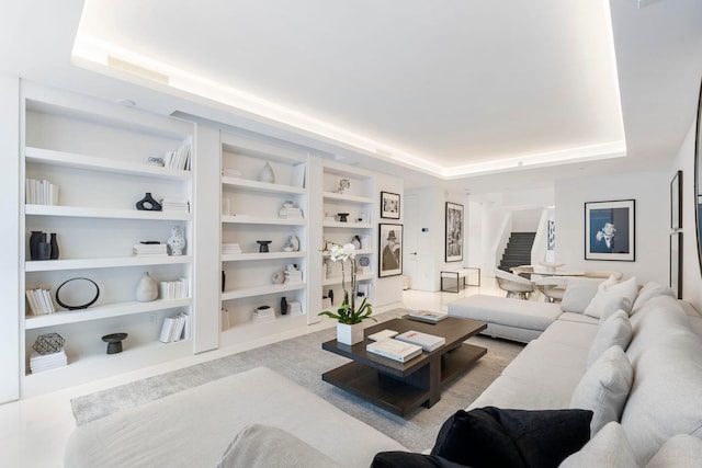 living room featuring light carpet, built in shelves, and a raised ceiling