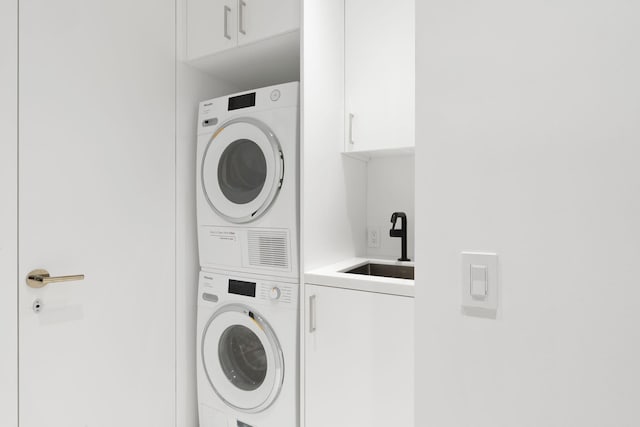 laundry area with sink, stacked washer and dryer, and cabinets