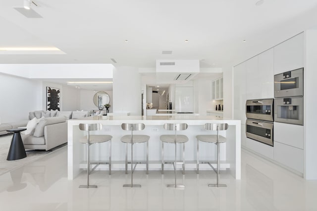 kitchen featuring a breakfast bar area, a large island with sink, white cabinets, and double oven