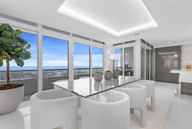 dining area featuring a water view, a raised ceiling, and light tile patterned flooring