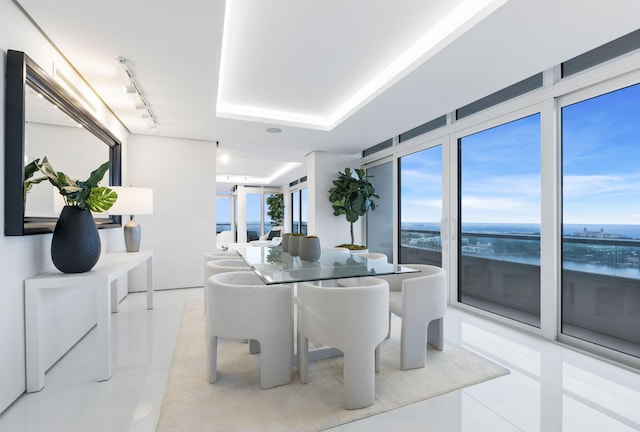 dining area with a water view, a tray ceiling, and light tile patterned flooring