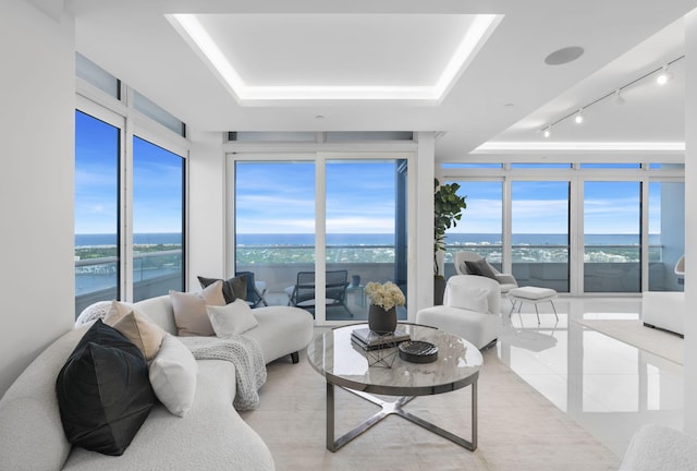 living room with a water view, track lighting, a tray ceiling, and floor to ceiling windows