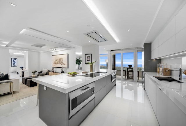 kitchen featuring gray cabinetry, sink, an island with sink, black electric cooktop, and light tile patterned floors