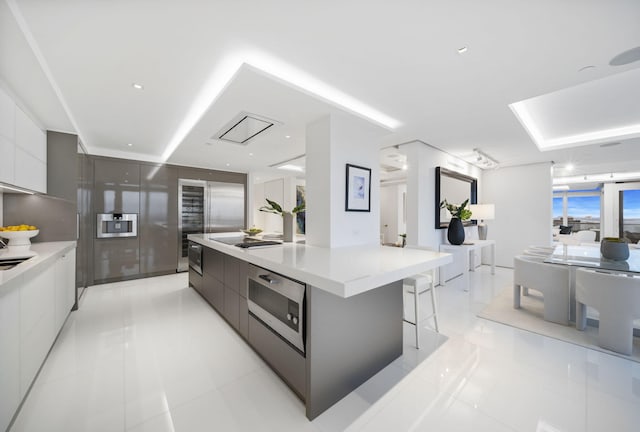 kitchen featuring a spacious island, black electric cooktop, a breakfast bar area, light tile patterned flooring, and white cabinets