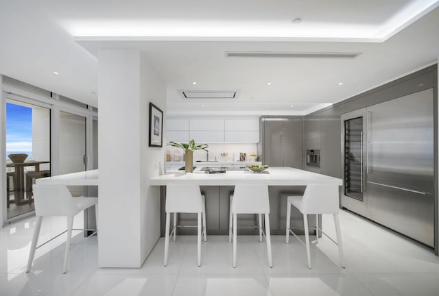 kitchen featuring kitchen peninsula, decorative backsplash, stainless steel built in fridge, light tile patterned floors, and a breakfast bar area