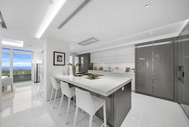 kitchen featuring decorative backsplash, light tile patterned floors, a kitchen island, white cabinetry, and a kitchen bar