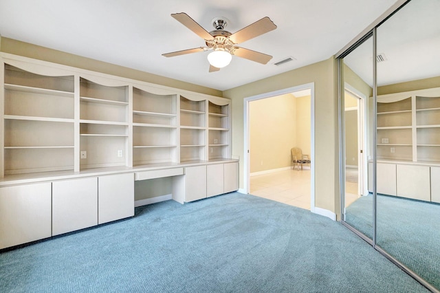 unfurnished bedroom with built in desk, light colored carpet, ceiling fan, and a closet