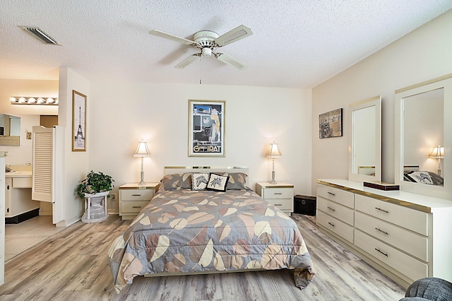 bedroom with ensuite bathroom, light wood-type flooring, a textured ceiling, and ceiling fan