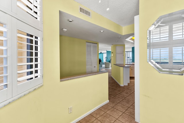 corridor with a textured ceiling and light tile patterned flooring