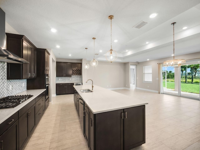 kitchen featuring sink, an island with sink, decorative light fixtures, dark brown cabinets, and stainless steel appliances