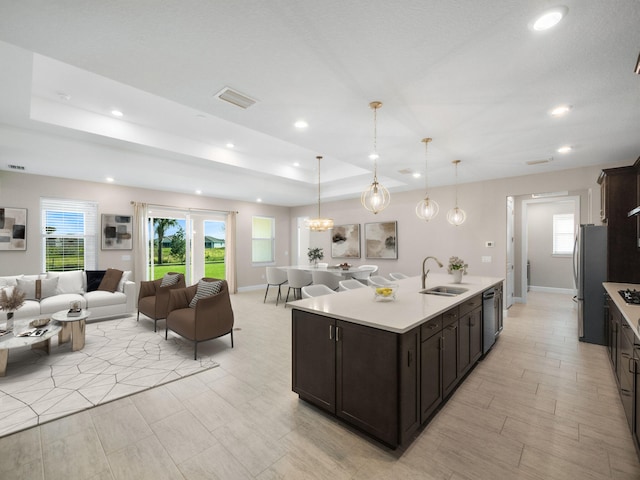 kitchen featuring appliances with stainless steel finishes, dark brown cabinetry, sink, a center island with sink, and hanging light fixtures