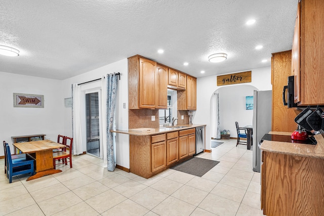 kitchen with appliances with stainless steel finishes, a textured ceiling, sink, and light tile patterned floors