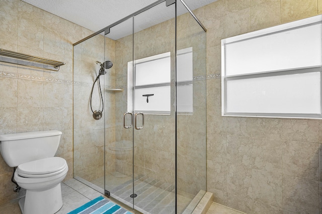 bathroom featuring a textured ceiling, a shower with shower door, toilet, tile patterned floors, and tile walls