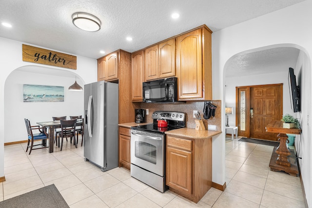 kitchen with a textured ceiling, decorative backsplash, stainless steel appliances, and light tile patterned flooring