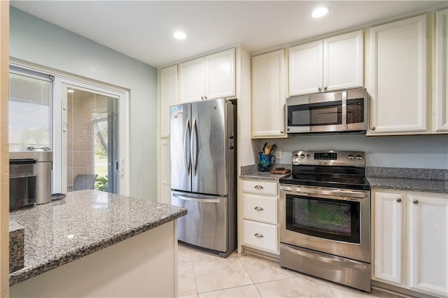 kitchen with appliances with stainless steel finishes, light tile patterned flooring, white cabinets, and stone countertops