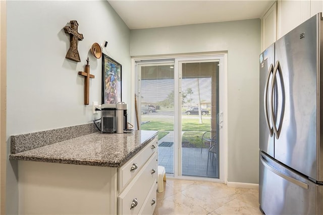 kitchen featuring stainless steel fridge, white cabinetry, and stone countertops